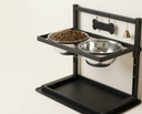 Black wall-mounted dog bowl rack with two steel bowls on a cream background