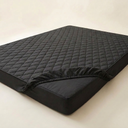 Quilted waterproof mattress protector fitted on a mattress on a cream background